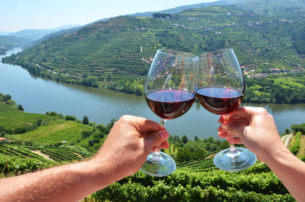 Dois copos de vinho a brindar com paisagem de fundo do Douro, Portugal